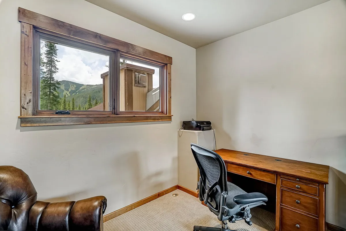 A dedicated home office space featuring a wooden desk, comfortable office chair, and a window offering breathtaking mountain views. The scene captures the focused, serene mood of working remotely in a tranquil environment inspired by nature.