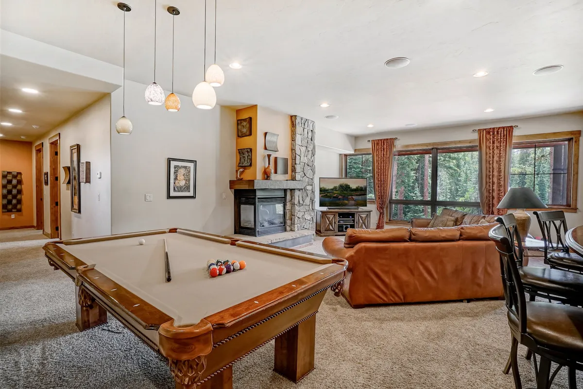 A spacious, open-plan entertainment area with a pool table, modern fireplace, large windows framing outdoor views, a comfortable sofa, and an adjacent dining area. The layout emphasizes opportunities for group activities, casual lounging, and enjoying scenic vistas from within the entertainment space.