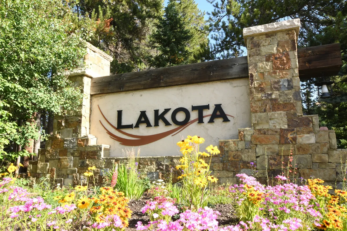 The property sign sits amidst colorful flowers and lush natural surroundings, marking the entrance and welcoming visitors. The scene radiates warmth and approachability, introducing the broader context of the property and its integration with the local landscape.