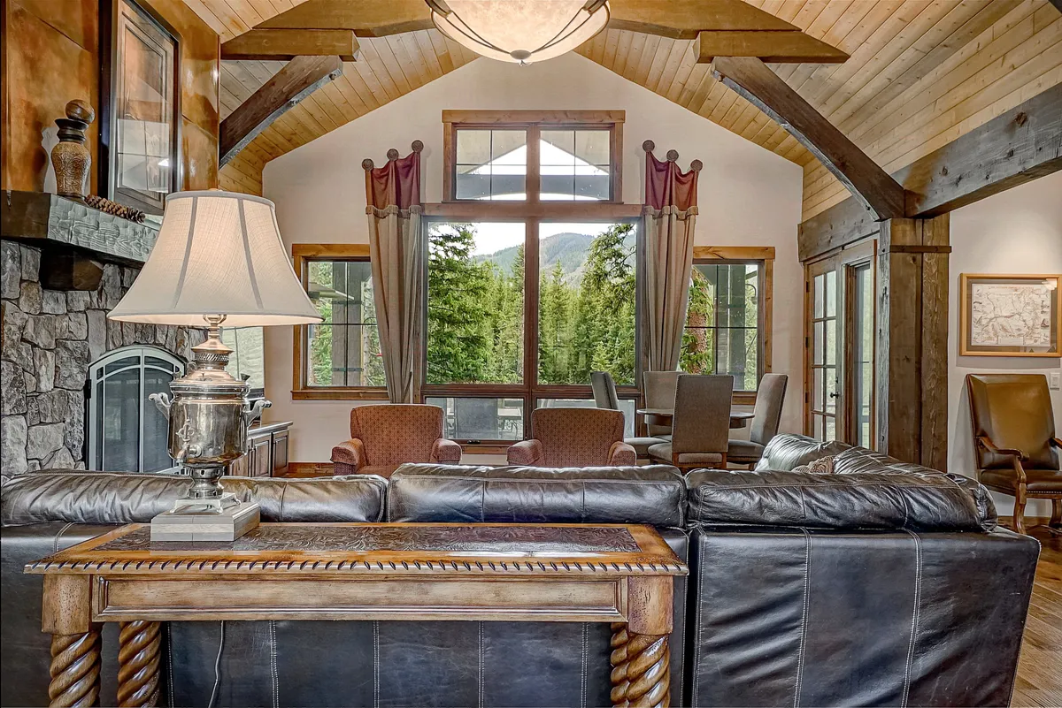 A living area with large windows framing scenic views, wooden beams, an elegant lamp, and a stone fireplace. The inviting space is designed for relaxation, gatherings, or simply enjoying the spectacular sunsets and natural light.