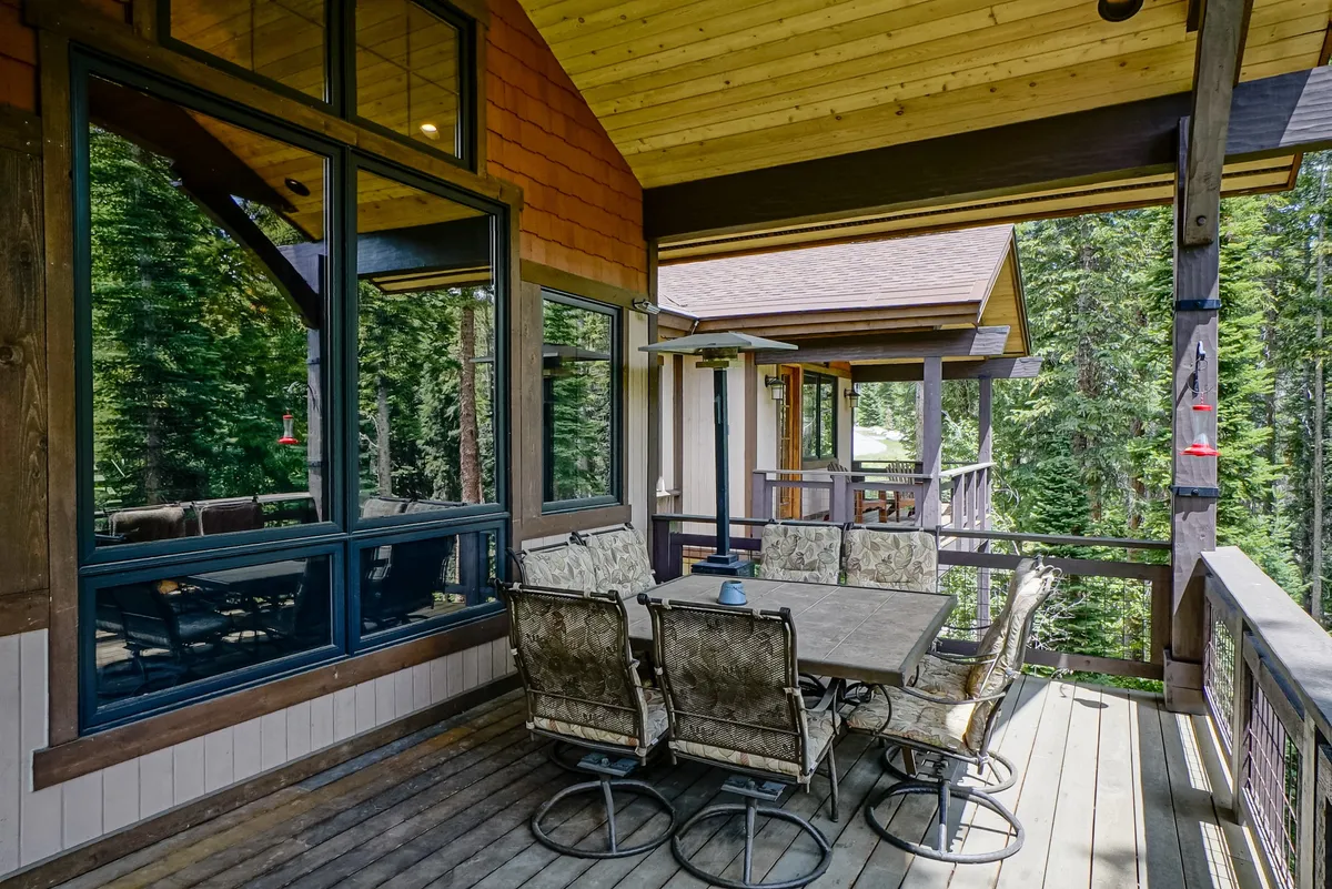 A serene outdoor patio set amidst lush trees, featuring a dining table with patio chairs and an outdoor heater. The setting is ideal for al fresco meals, relaxing with morning coffee, or gathering with friends in the fresh mountain air. Warm sunlight filters through the foliage, enhancing the tranquil and inviting ambiance.