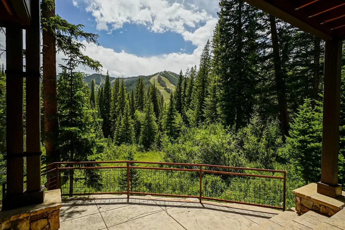 A tranquil patio scene with a secure railing overlooks a dense forest and the majestic mountains beyond. The setting is ideal for enjoying sunrises, sunsets, or simply soaking in the serene atmosphere.