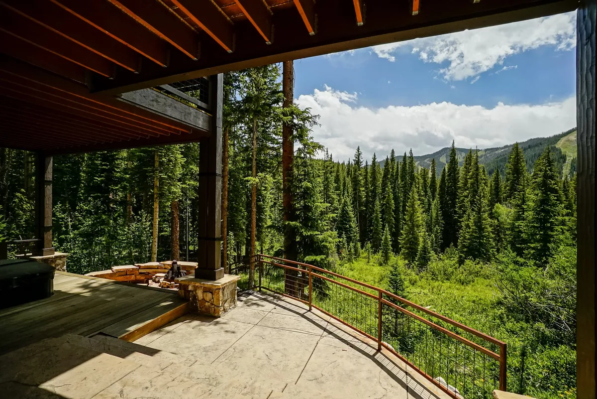 This image showcases an open wooden deck with sturdy beams, surrounded by forest and offering expansive mountain views. The space is outfitted for relaxation and socializing, inviting guests to experience peaceful moments outdoors while connecting with the natural setting.
